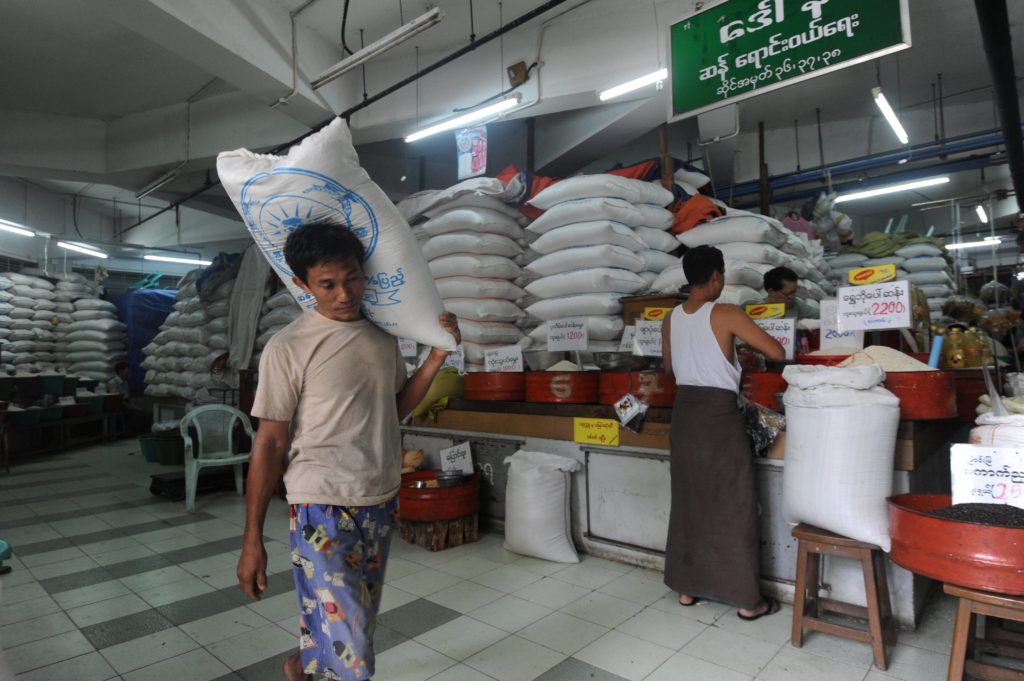 To go with Myanmar-lifestyle-economy-rice, FEATURE by Jerome Taylor and Nan Tin Htwe In this picture taken on April 6, 2015, a worker carries a sack of rice past a stall selling the grain at a market in Yangon. For much of the early 20th century Myanmar was Asia's rice bowl, but after a nominally socialist junta seized power in 1962, decades of mismanagement shattered the agriculture industry in a nation where 70 percent of inhabitants still live in the countryside. The quasi-civilian reformist government, which took over from the military in 2011, is determined to resurrect the country's reputation as a rice producer. AFP PHOTO / SOE THAN WIN / AFP PHOTO / Soe Than WIN